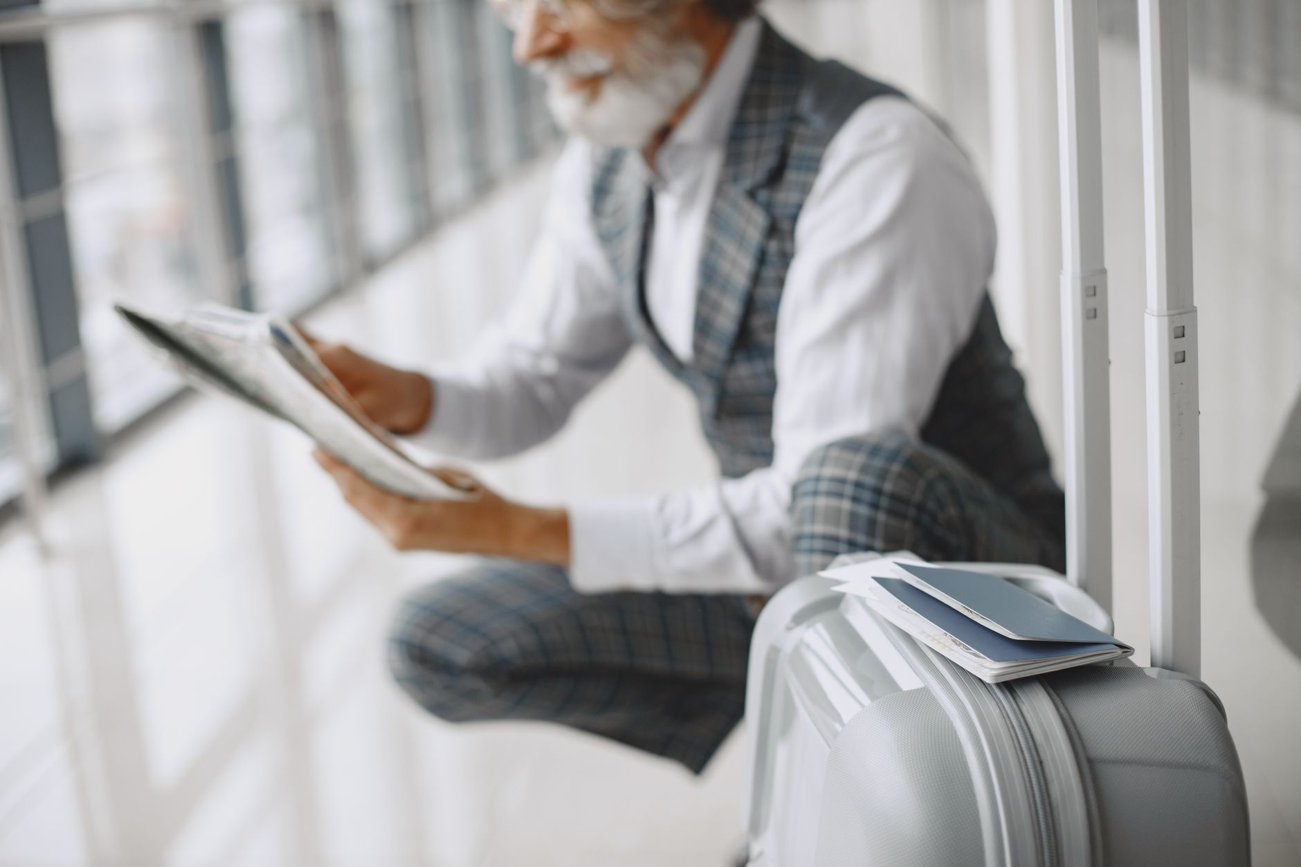 Older man in vest and white shirt sitting by window reviewing travel documents