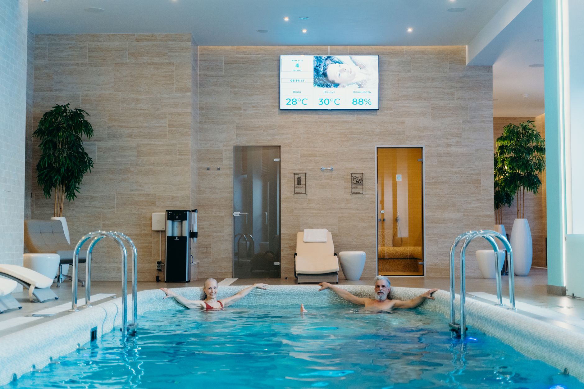Couple relaxant dans une piscine intérieure moderne avec affichage de température et humidité.