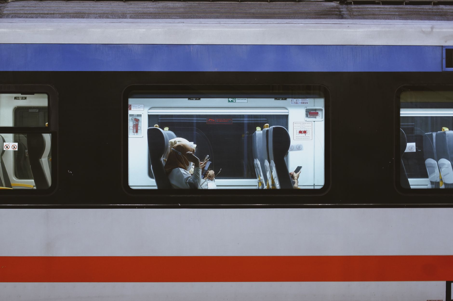Fahrgäste sitzen in einem modernen Zug mit blauer und roter Farbgebung.