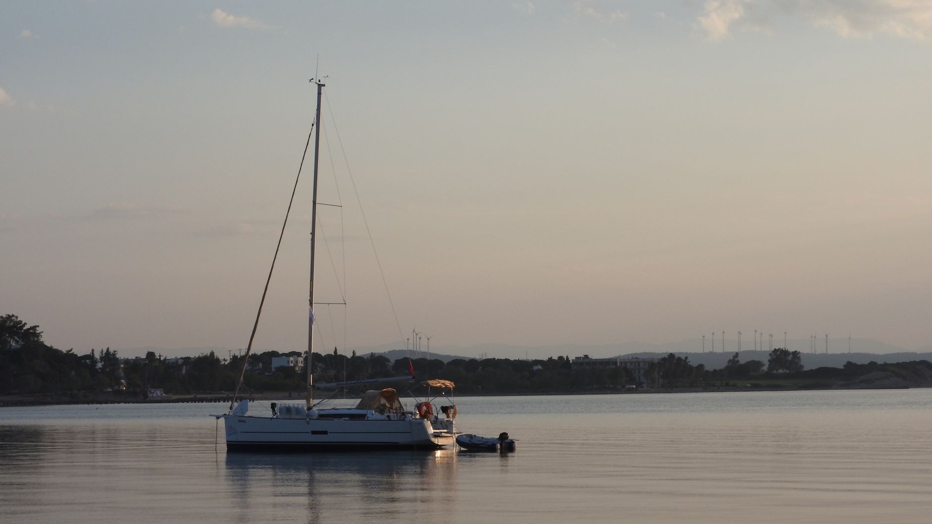 Ein weißes Segelboot ankert in ruhigem Wasser mit Baumsilhouetten im Hintergrund
