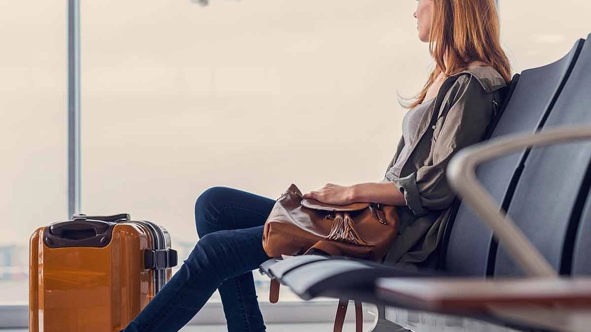Woman with red hair sitting in airport lounge with brown luggage and shoulder bag