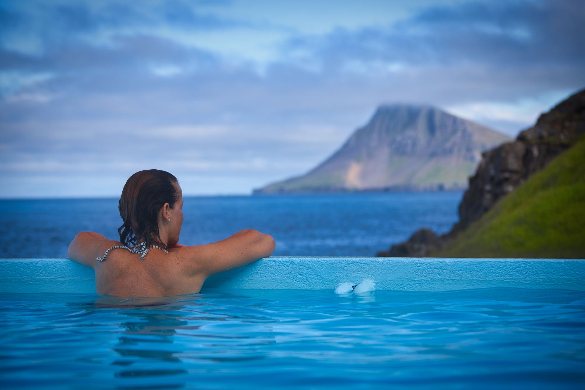 Femme détente dans une piscine extérieure face à la mer et montagnes côtières.