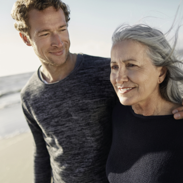 Man and older woman smiling together on beach at sunset