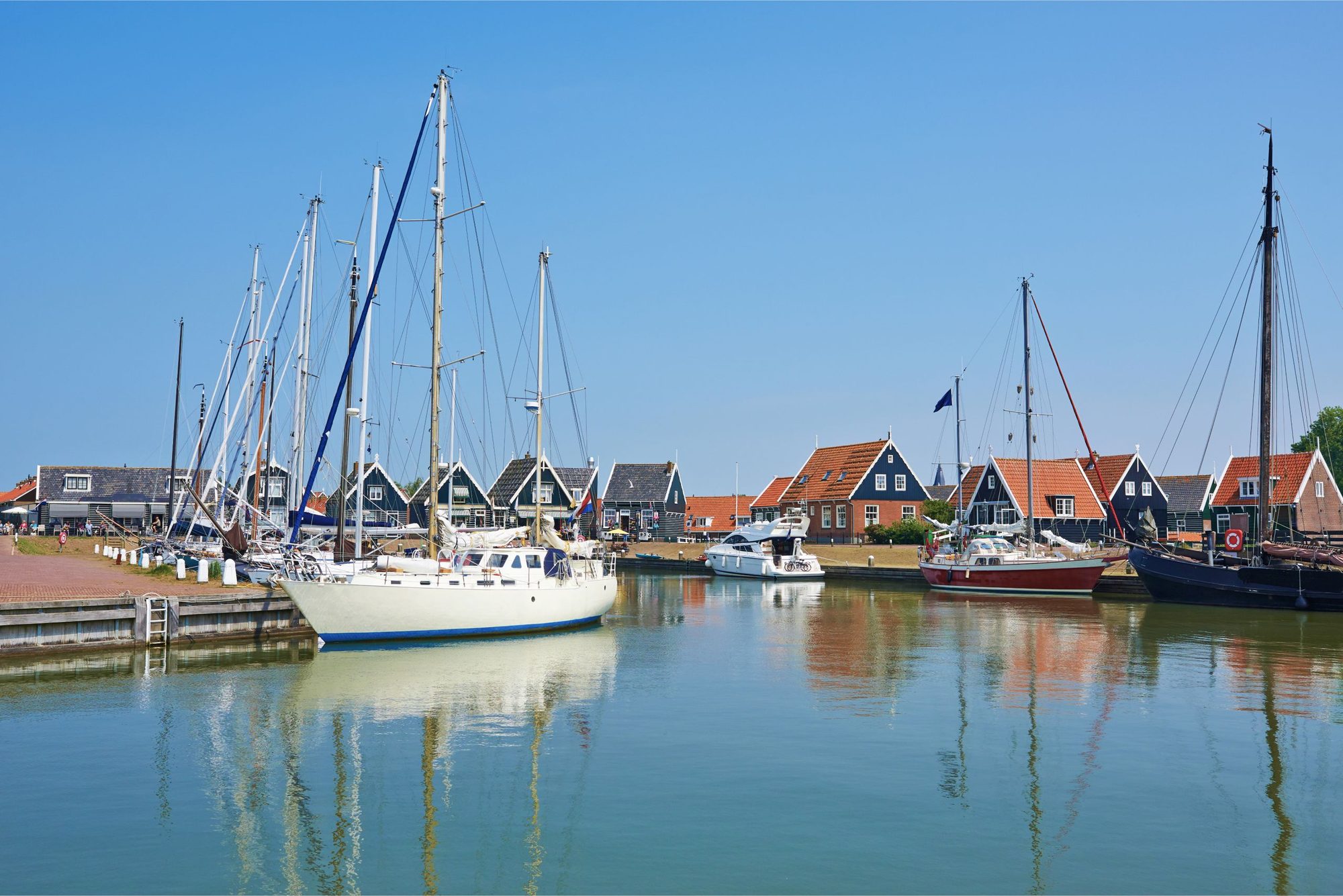 Mehrere Segelschiffe mit hohen Masten liegen in einem Hafen vor niederländischen Häusern mit roten Dächern