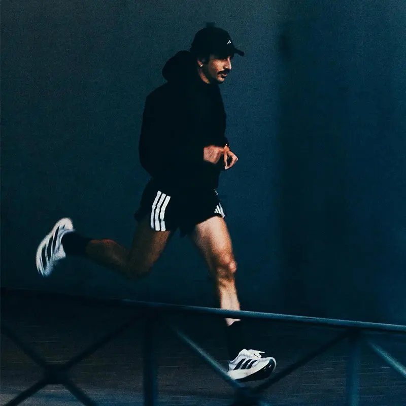 Coureur en tenue noire et shorts Adidas blanc avec rayures, portant des chaussures de running blanches