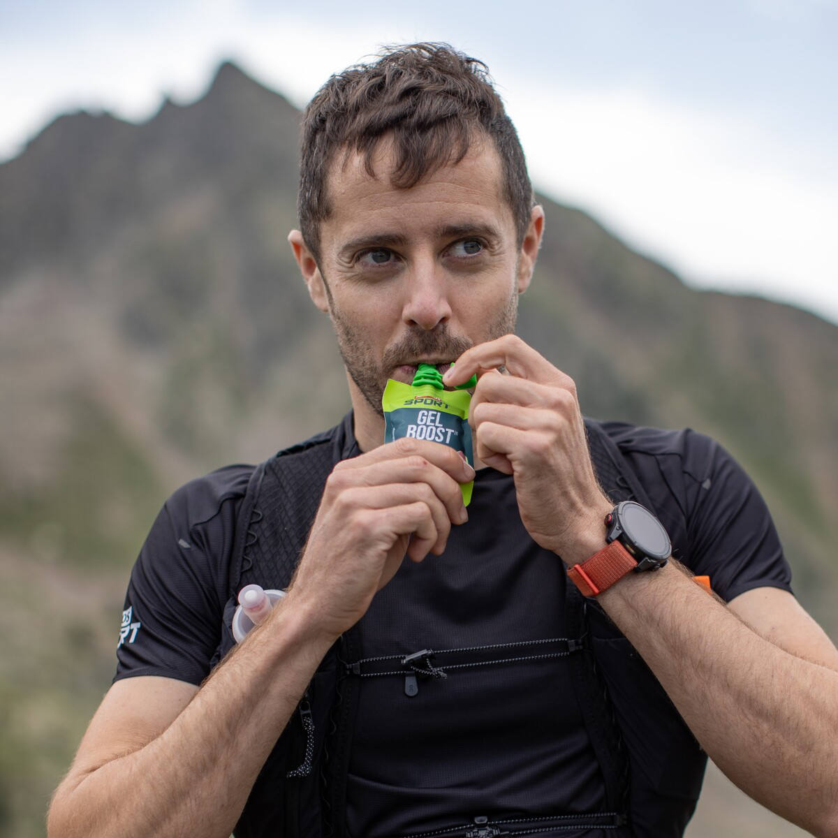 Coureur en tenue de sport noir consomme un gel énergétique en montagne