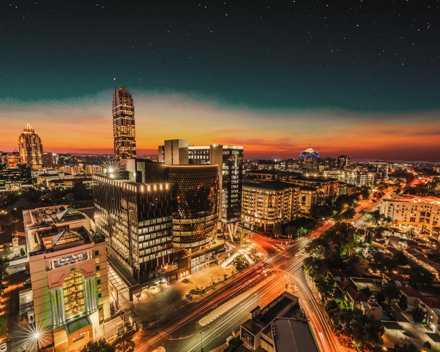 Urban cityscape at dusk with illuminated skyscrapers, light trails from traffic, and starlit sky above