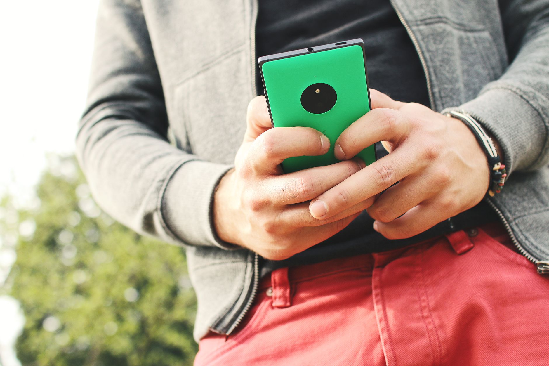 Person in casual jacket holding a green smartphone outdoors with trees in background