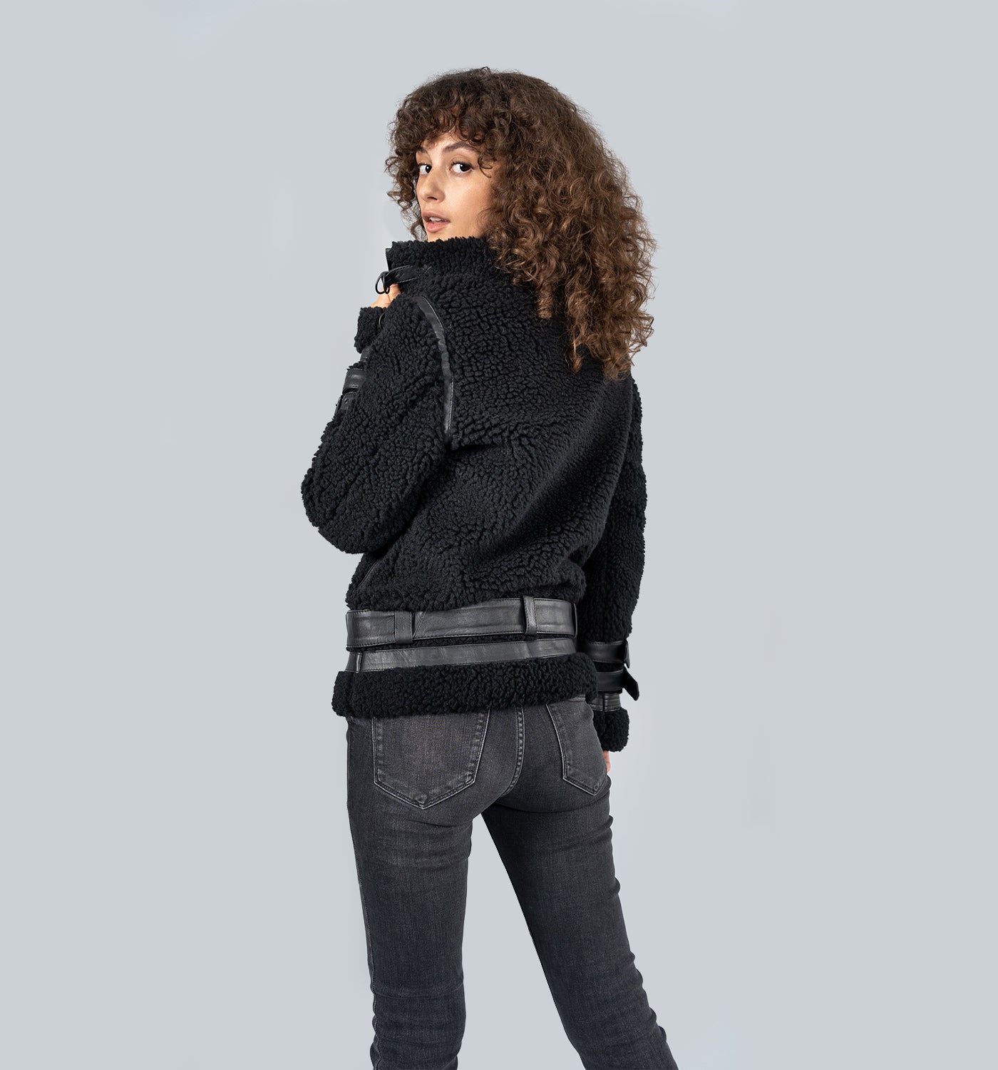 Rückansicht: Mädchen in schwarzer Wollvlies-Jacke mit grauem Gürtel und Jeans