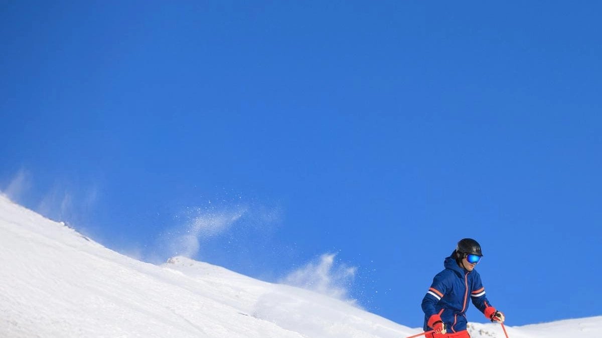 Child in blue ski jacket and goggles skiing down snowy mountain slope under clear blue sky