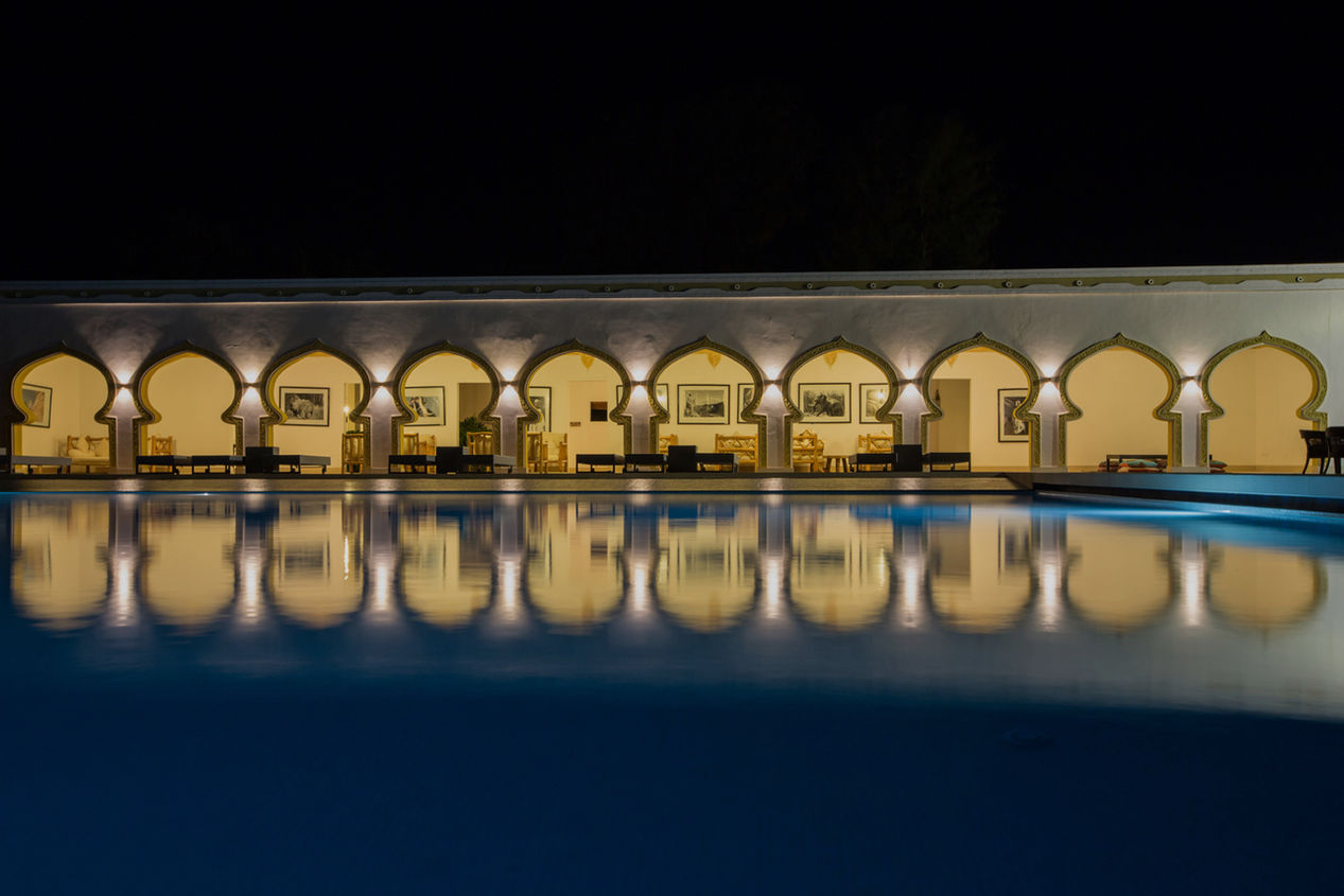 Row of illuminated Moroccan-style archways reflected in still water at night against dark sky