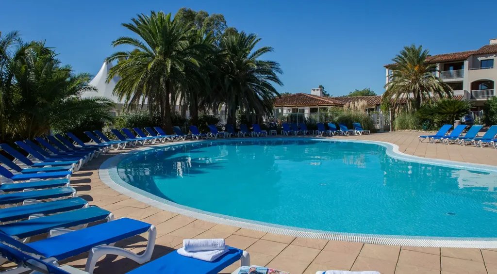 Piscine turquoise bordée de palmiers et de chaises longues bleues en resort.