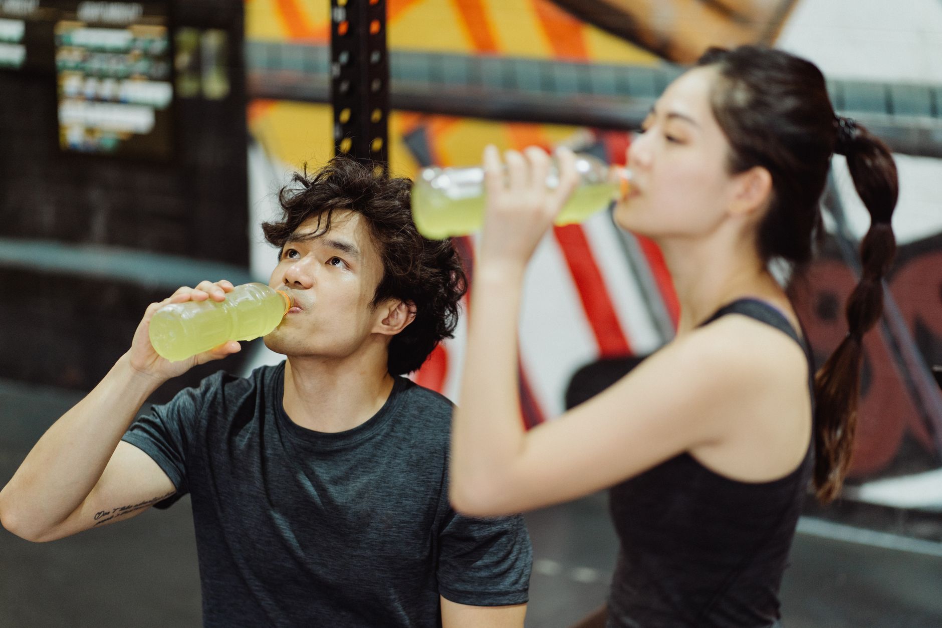 Zwei Sportler trinken Getränke in einer Sporthalle während des Trainings.