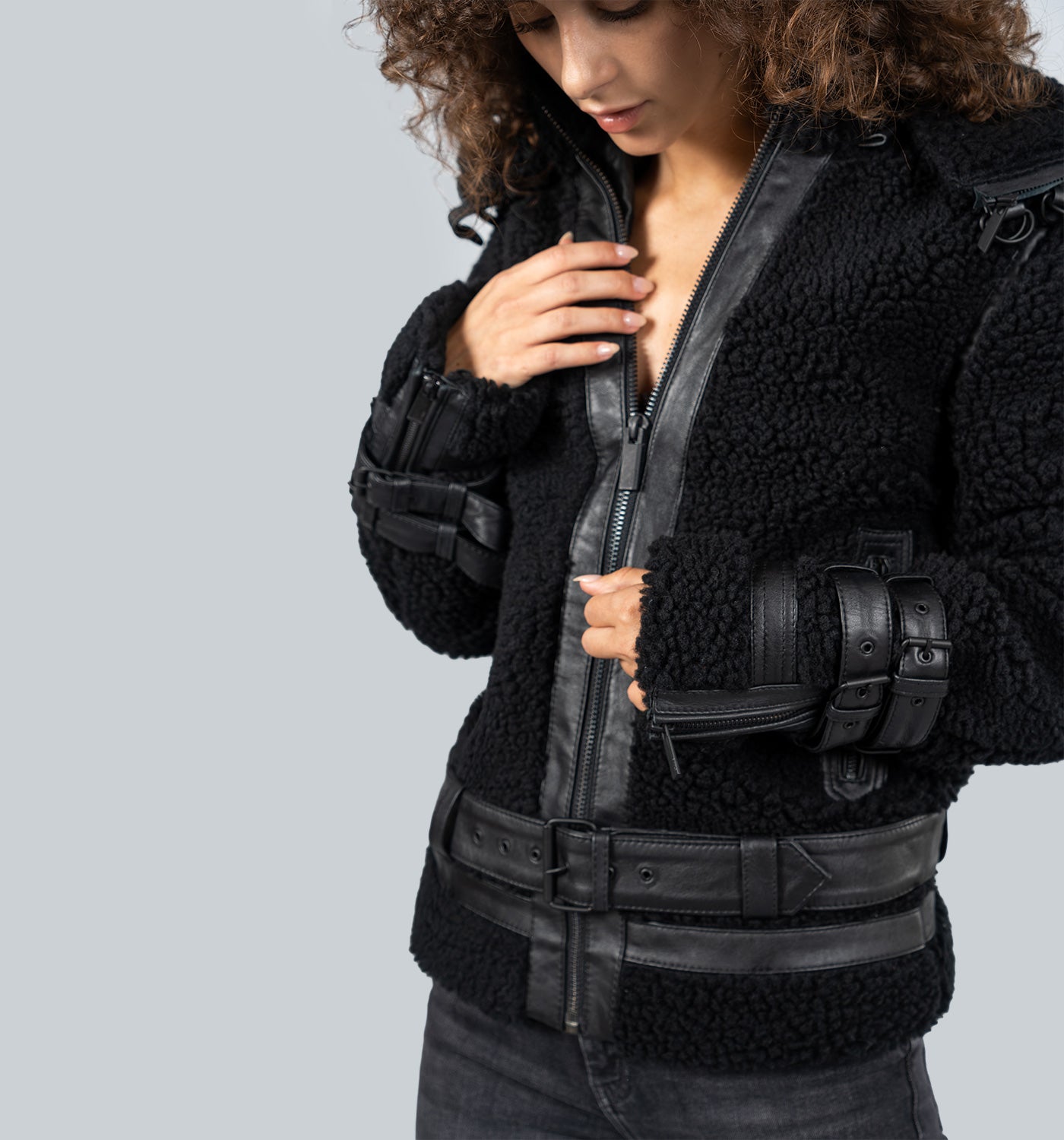 Mädchen mit lockigen braunen Haaren trägt schwarze Lederjacke mit Reißverschluss und Gürtel