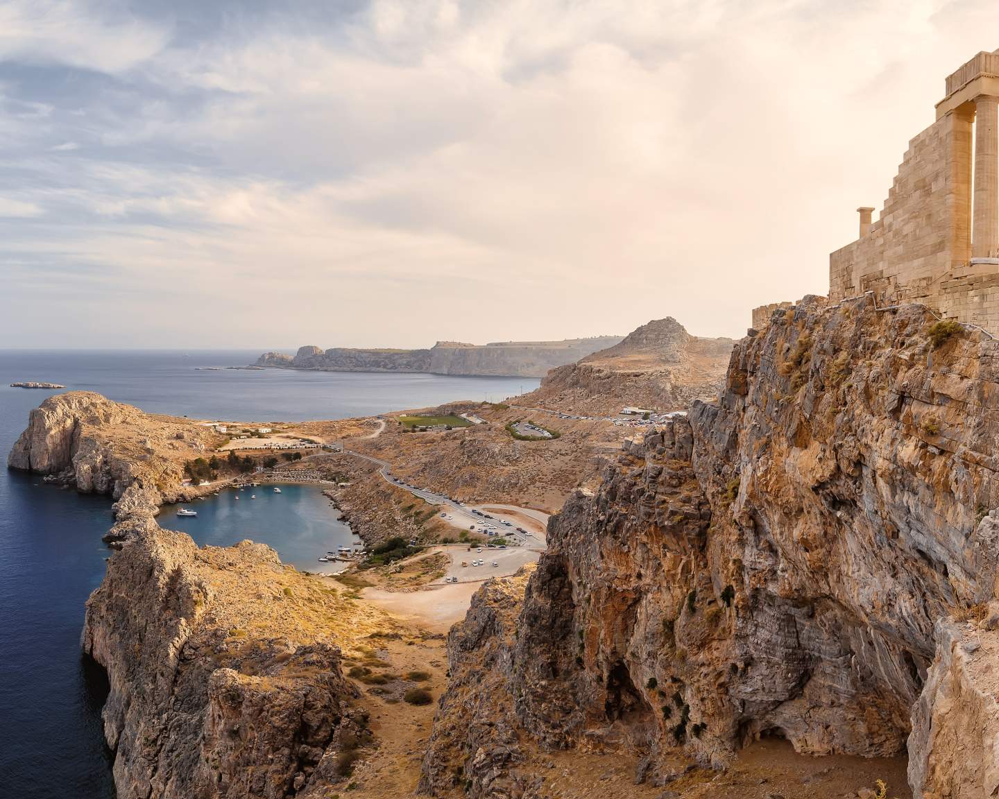 Rocky Mediterranean cove with ancient Greek temple ruins perched on clifftop overlooking turquoise sea