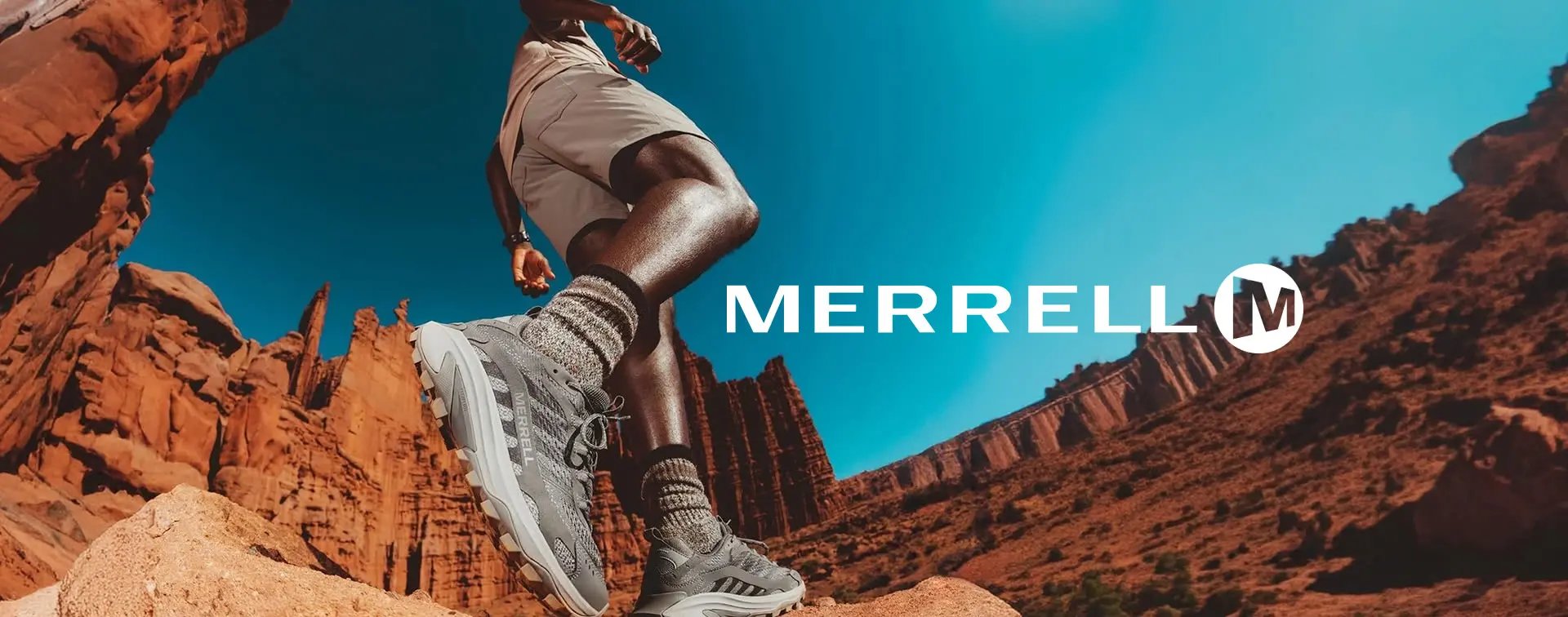 Coureur au-dessus d'un canyon rocheux en short beige et chaussettes de compression, portant des chaussures de trail gris clair