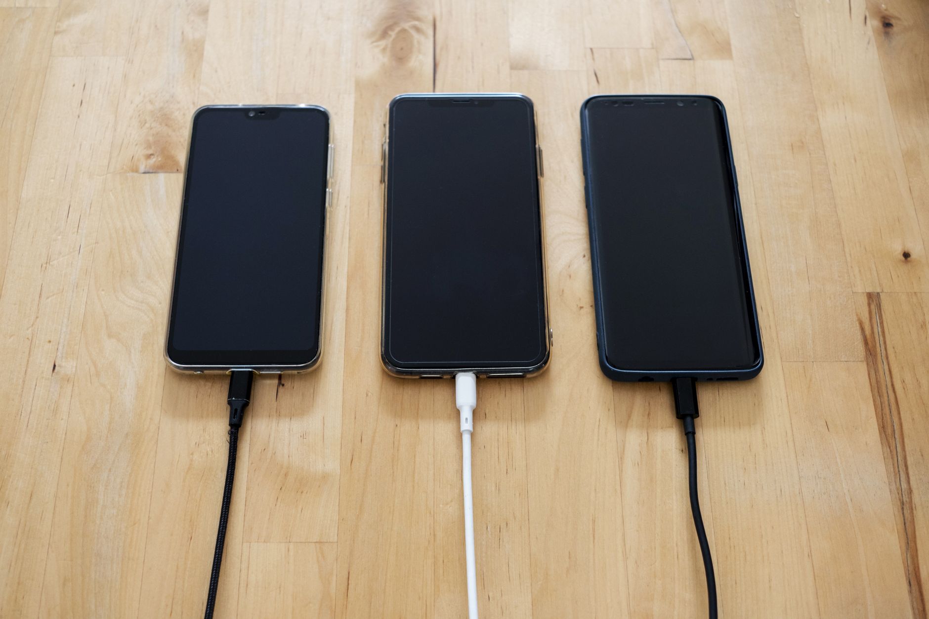 Trois téléphones intelligents alignés sur du bois avec des câbles de chargement noirs et blanc.